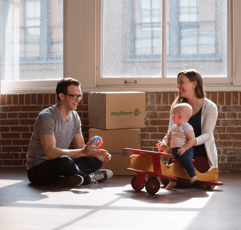 young couple sitting on the floor playing with their child with boxes in the background- Mayflower®