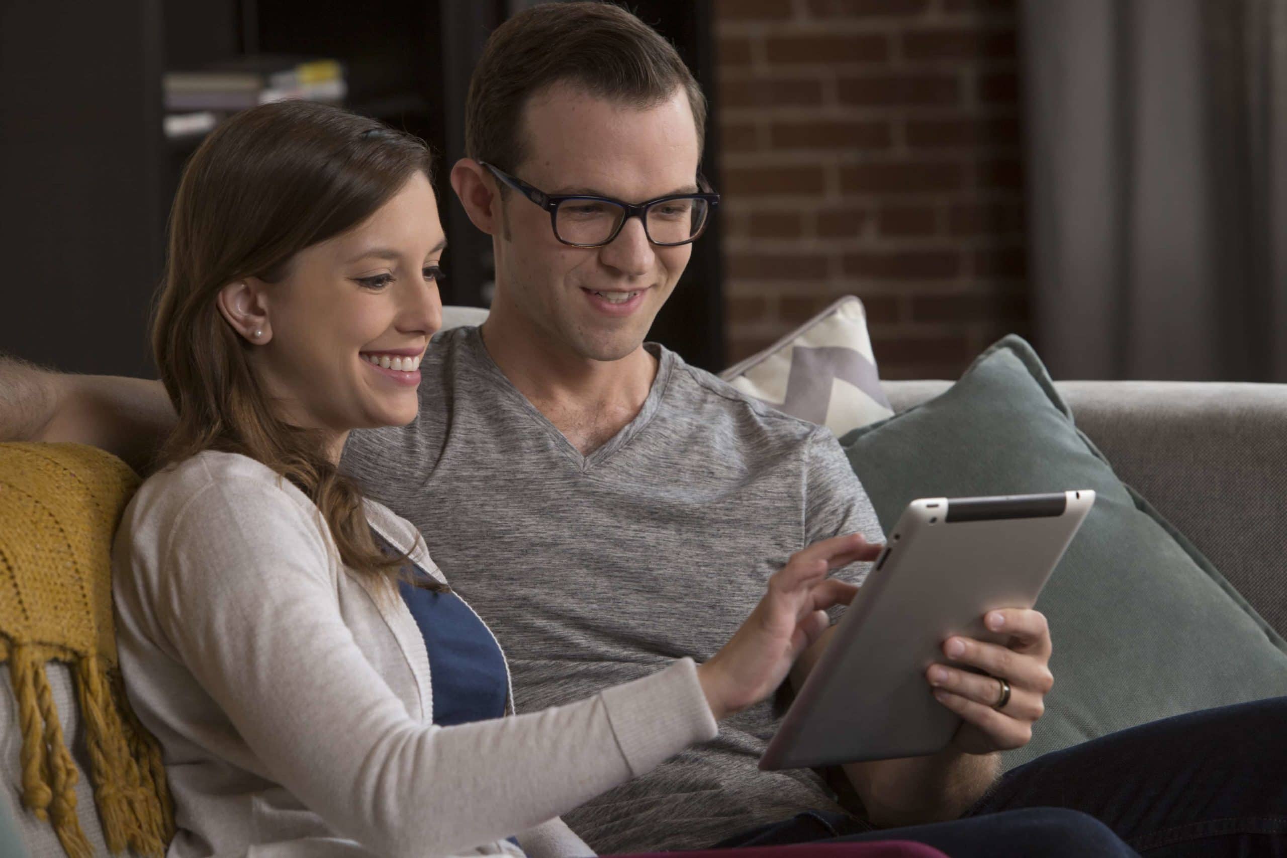 a couple holding a tablet sitting on a couch - Mayflower®