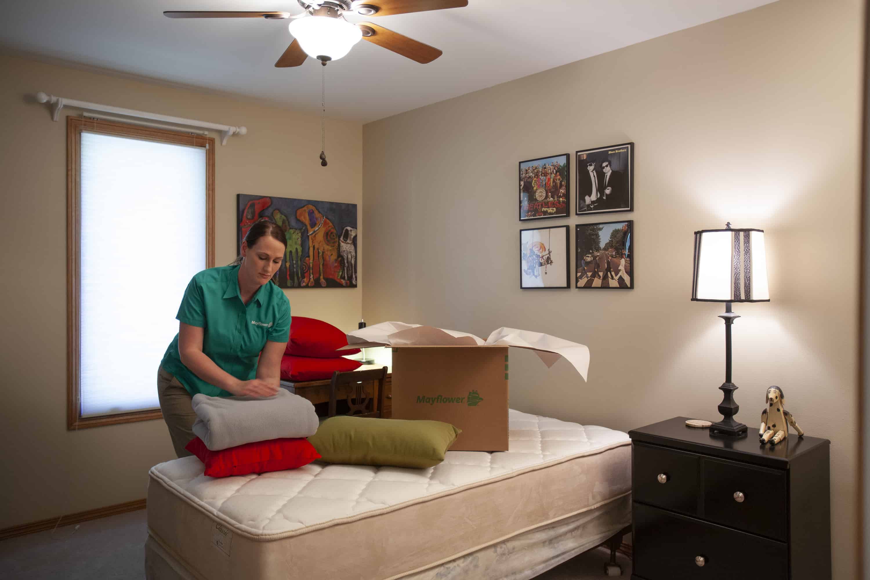 How To Pack Your Bedroom - woman mover packing blankets on a stripped bed into boxes- Mayflower