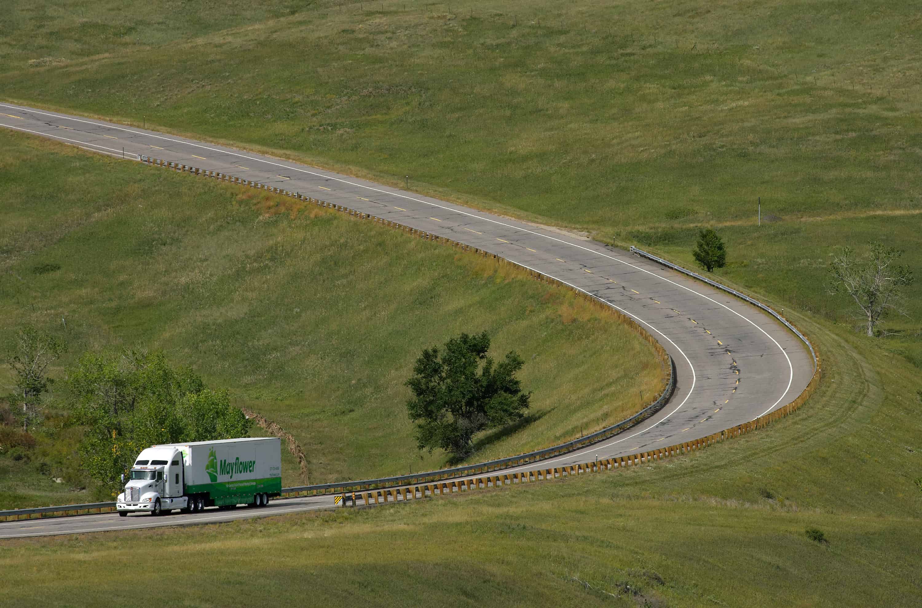 Mayflower moving truck driving down a rural highway surrounded by grassy areas