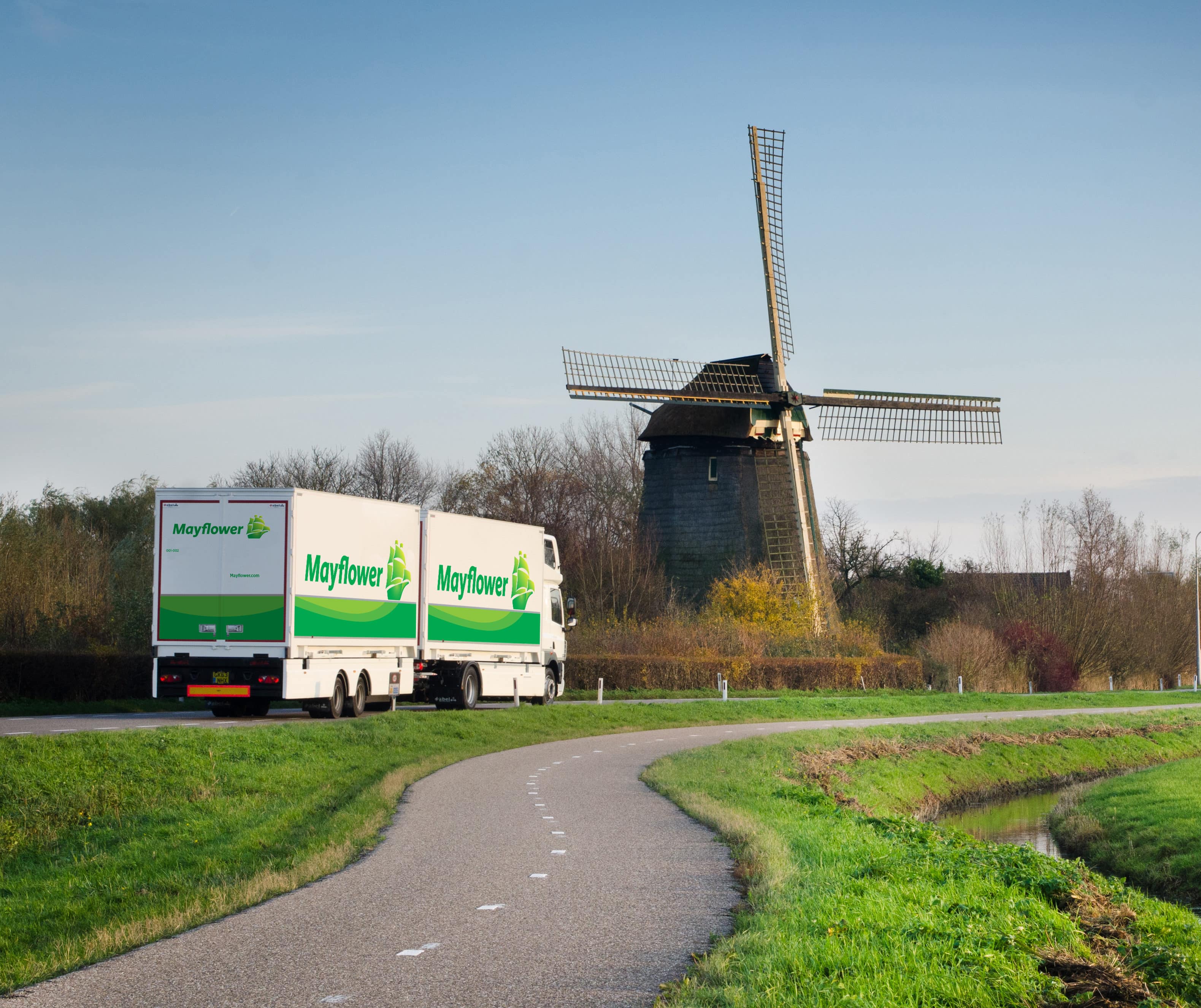 International Movers - Mayflower truck driving down a rural road passing a wooden windmill - Mayflower®