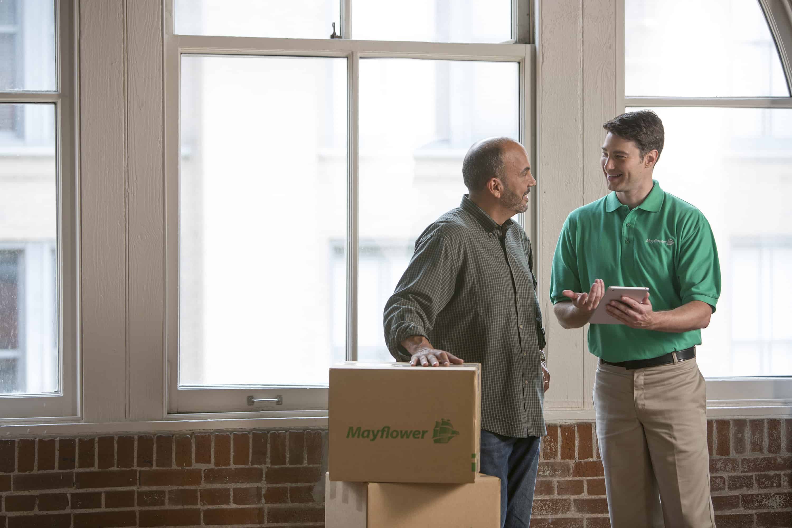 customer speaking with Mayflower mover in front of a window with his hand resting on a stack of moving boxes - Mayflower®