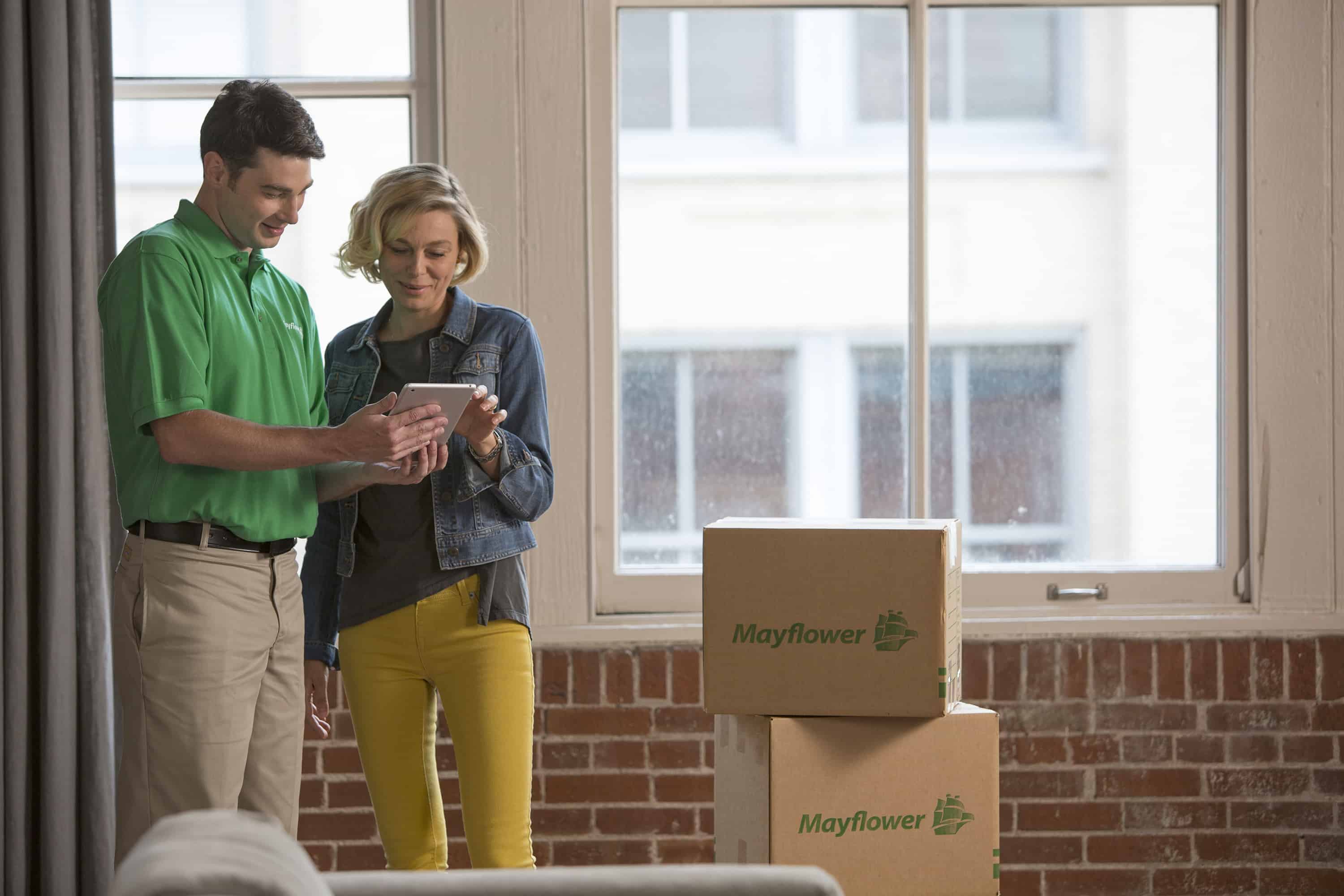 Understanding Moving Costs - male mover and female customer in an urban setting looking at a quote on a tablet with moving boxes in the background - Mayflower