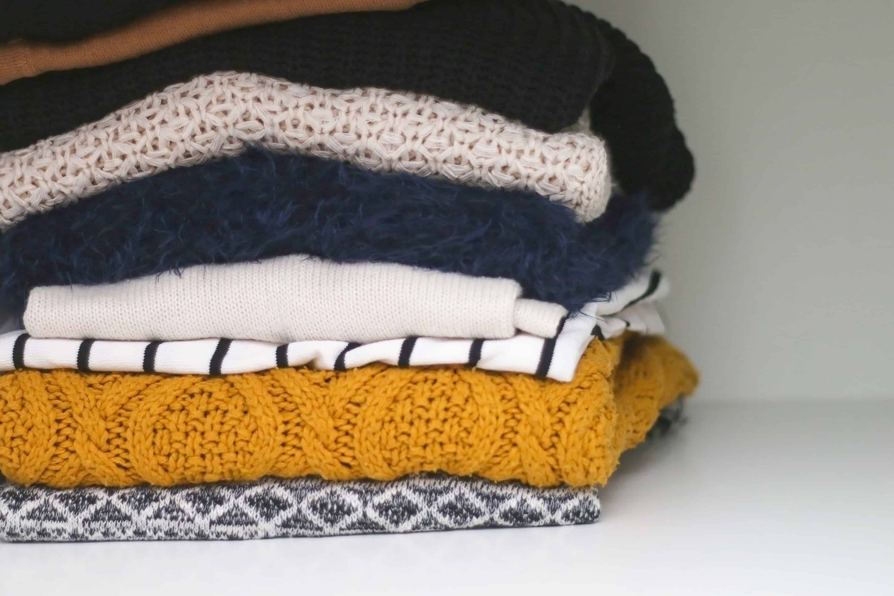 How to Pack Your Clothes - Pile of various sweaters in the closet. Selective focus. - Mayflower
